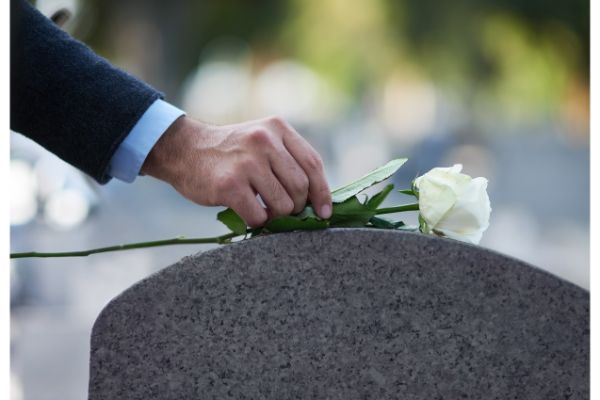 man placing rose on a tombstone